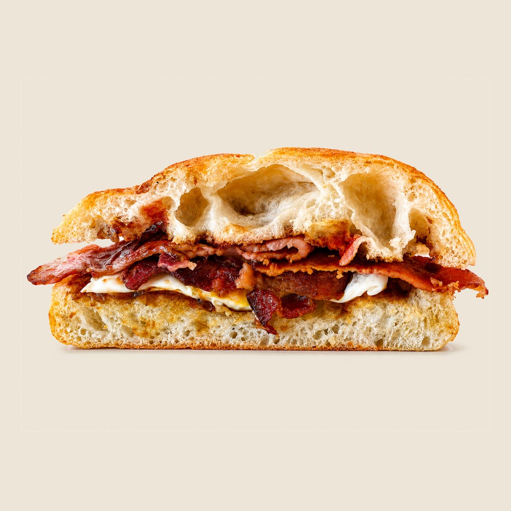 Bacon and egg roll on a crusty white roll, cut through to show the bacon and fried egg.