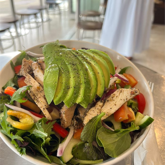 Grilled chicken salad with sliced avocado, tomato, cucumber and mixed leaves in a white bowl.