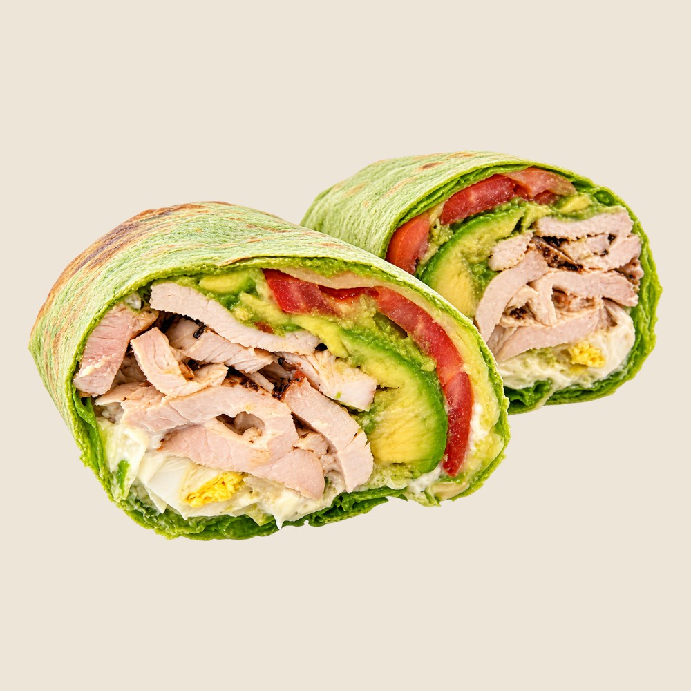 Grilled chicken wrap in a spinach tortilla, cut in half to show chicken, avocado, tomato and egg.