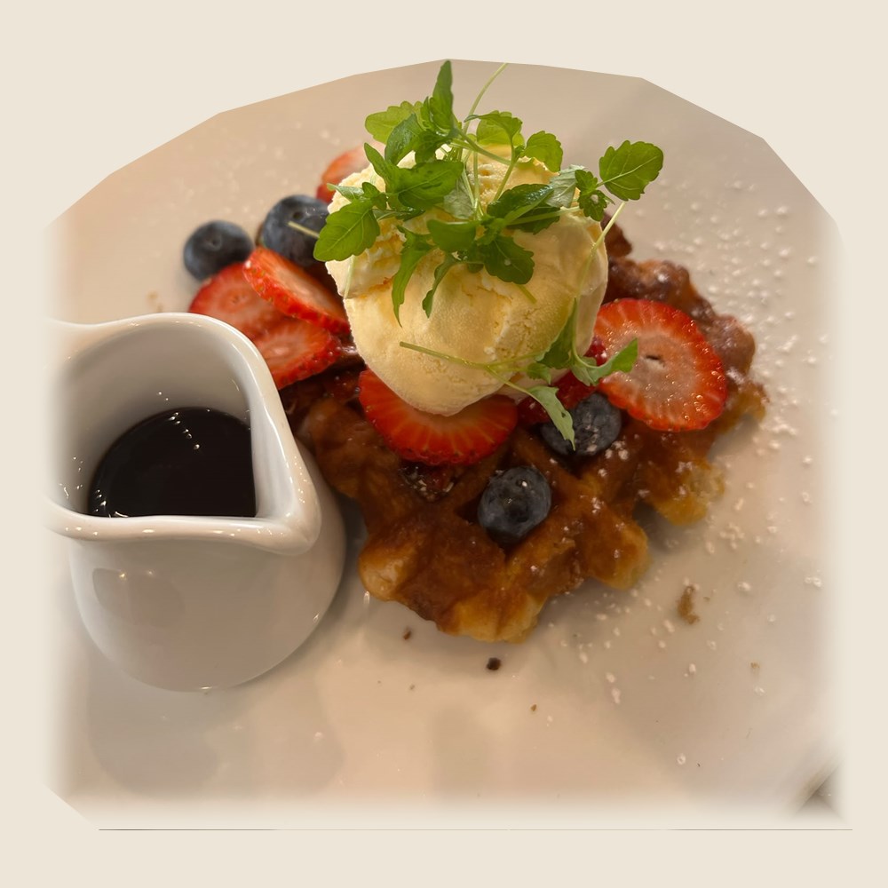Belgian chocolate waffle topped with vanilla ice cream, strawberries, blueberries and mint, with a jug of chocolate sauce.